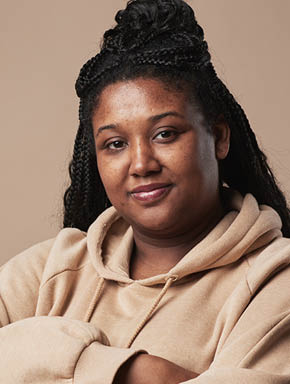Minimal waist up portrait of confident curvy woman looking at camera and wearing comfortable hoodie while standing with arms crossed against neutral beige background in studio, copy space