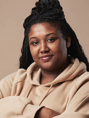 Minimal waist up portrait of confident curvy woman looking at camera and wearing comfortable hoodie while standing with arms crossed against neutral beige background in studio, copy space